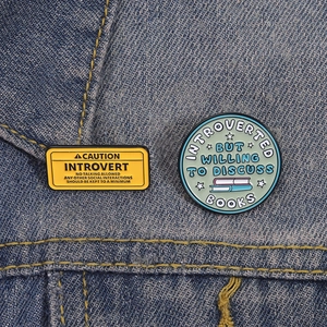 Funny enamel pin set for introverts and book lovers pinned on a blue denim jacket