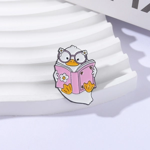 Cute enamel pin featuring a white duck reading a pink book with floral accents