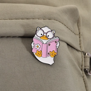 Macro shot of cute enamel duck pin reading a pink book on a fabric backpack background