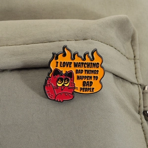 Pin's chat démon rouge avec flammes sur sac à dos vert avec slogan textuel cynique