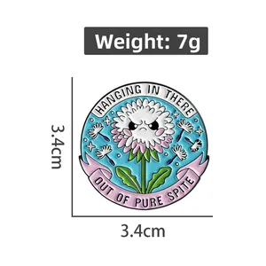 Detail view of dandelion enamel pin with size 3.4cm and text hanging in there out of pure spite