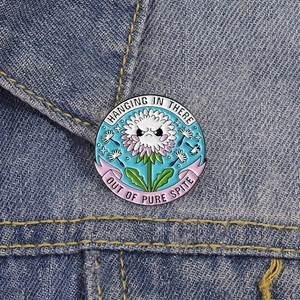 Funny dandelion enamel pin with hanging in there slogan on blue denim jacket