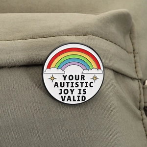 Detail van ronde emaille badge met regenboog en YOUR AUTISTIC JOY IS VALID tekst op canvas