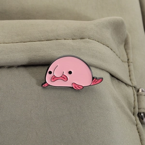 Nahaufnahme einer rosa Blobfisch-Emaille-Anstecknadel an einem khakifarbenen Rucksack