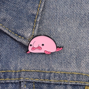 Cute pink blobfish enamel pin on denim background, funny cartoon brooch accessory