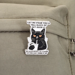 Close-up of black cartoon cat enamel pin with a drink quote on a canvas backpack