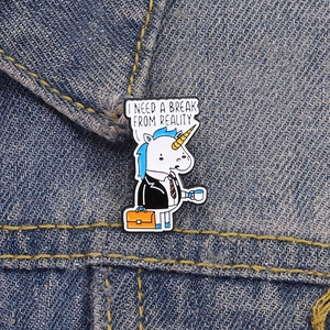 Détail du pin's émaillé licorne avec café et mallette sur un fond en tissu denim bleu