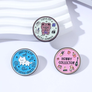 Three cute round enamel hobby badges with animal and slogan designs on a white platform
