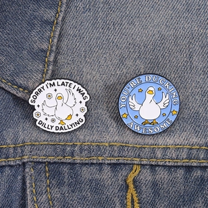 Close-up of duck enamel pins with fun quotes pinned to a classic blue denim jacket