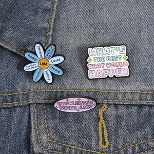 Set of three floral and rectangular motivational enamel pins on a denim jacket