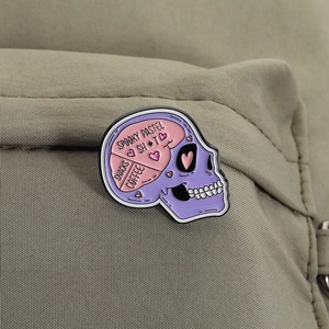 Macro shot of Pastel Goth skull enamel pin with Spooky Pastel text on green fabric
