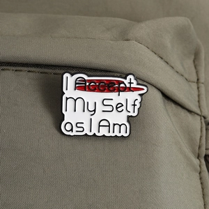 Detail der 'I Accept My Self as I Am' Emaille-Anstecknadel auf einem khakifarbenen Rucksack