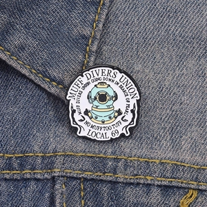 Detailansicht des Muff Divers Union Emaille-Ansteckers auf dunklem Denim-Gewebe