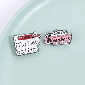 Modern enamel pins featuring self-acceptance and feedback rejection quotes on a teal plate