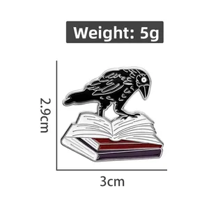 Vue détaillée de la broche corbeau en émail sur des livres, dimensions 2,9 cm par 3,0 cm