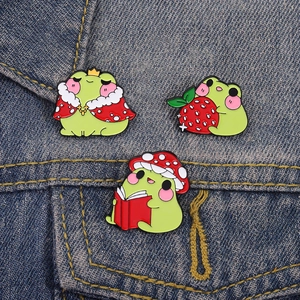 Three-piece cute frog enamel pin set with strawberry and mushroom designs on denim jacket