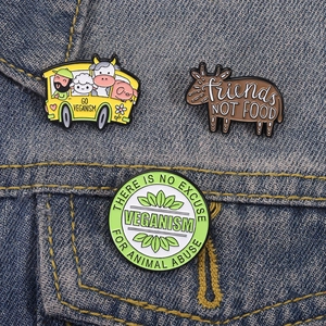 Vegan enamel pins featuring animal bus and slogan on blue denim fabric background
