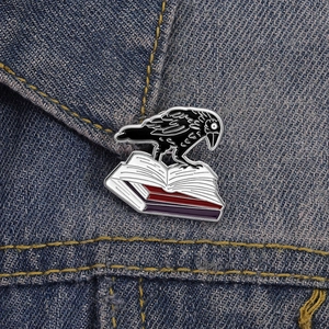Broche en émail corbeau noir sur des livres épinglée au col d'une veste en jean bleu foncé