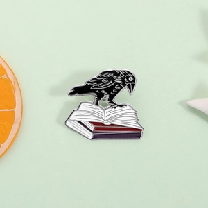 Broche en émail corbeau sur livres pour style vestimentaire gothique et sombre