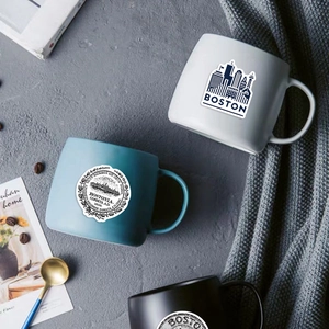 Macro shot of Boston skyline and seal stickers on matte ceramic coffee mugs in a cozy setting