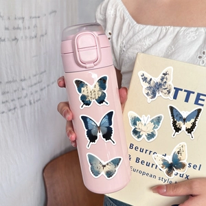 Detalle de pegatinas de mariposas estilo tinta en taza térmica y portada de cuaderno