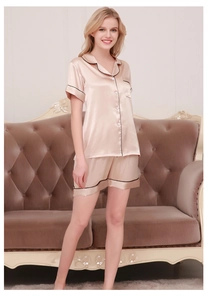 Detail of champagne silk pajamas set showing contrast piping and satin texture on a sofa