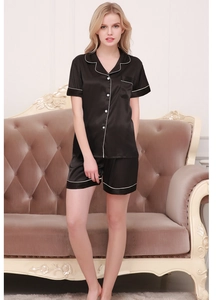 Detail view of women's black satin sleepwear set with white piping on the sofa