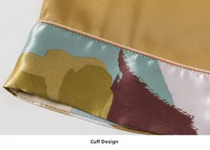 Close-up of golden silk pajama cuff with abstract print and pink piping detail