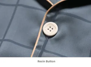 Close-up of a white four-hole resin button with gold trim on grey checkered silk pajamas