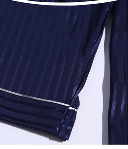 Detailed close-up of navy blue striped silk pajamas featuring white piping and satin finish
