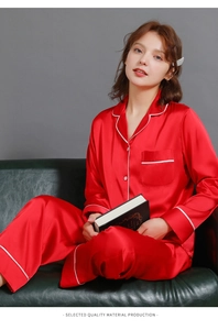 Detail of red silk pajama set with white piping and breast pocket on a luxury sofa