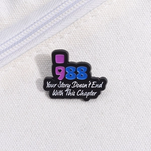 Detailed close-up of 988 enamel pin with inspirational text on white fabric texture