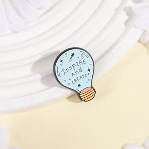 Dettaglio macro della spilla smaltata Inspire and Create su scale decorative bianche