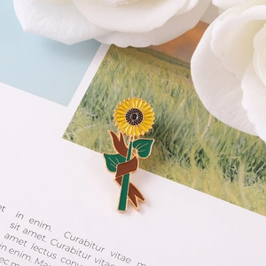 Artistic yellow sunflower enamel brooch with green stem on a magazine background