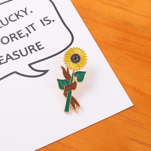 Vibrant sunflower enamel pin with yellow petals and green leaves on an orange background