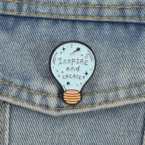 Dettaglio della spilla a lampadina azzurra con slogan creativo su giacca di jeans