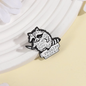 Funny cartoon raccoon enamel pin holding a knife with I Require Snacks text badge