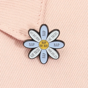 Detail of blue enamel daisy brooch with playful slogans on pink denim fabric background