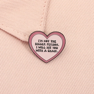 Detailed close-up of a pink heart enamel pin with humorous text on fabric