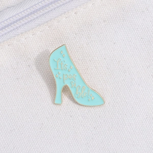 Detailed macro view of light blue high heel enamel pin with gold It's possible text