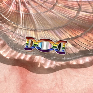 Macro detail of rainbow DNA helix enamel brooch on a shiny iridescent shell plate