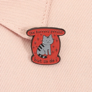 Détail du pin's émaillé chat gris sur tissu avec citation inspirante et bordure rouge