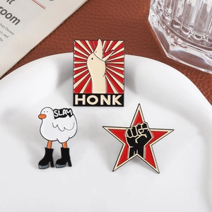 Three metal enamel pins featuring cartoon white geese and a fist icon on a white tray