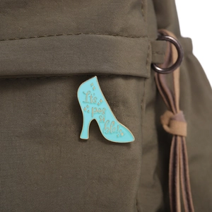 Detail of blue high heel enamel brooch with It's possible text on green canvas bag