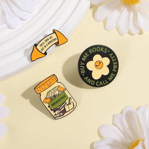 Three-piece metal enamel pin set with book and flower themes on a warm display
