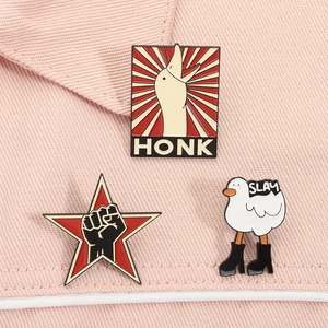 Close-up of enamel pins set featuring Honk goose and Slay duck on pink fabric
