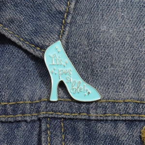 Teal high heel enamel pin with It's possible text on denim jacket lapel