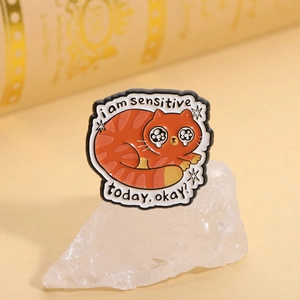 Detail of an orange cat enamel pin with I am sensitive today text on warm background