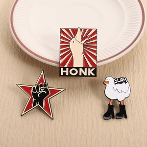 Set of funny enamel goose pins with HONK and SLAY text on a white ceramic plate