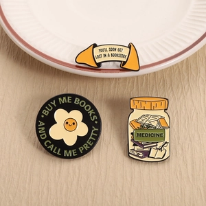 Detail view of book-themed enamel pins including medicine jar and lucky cookie designs
